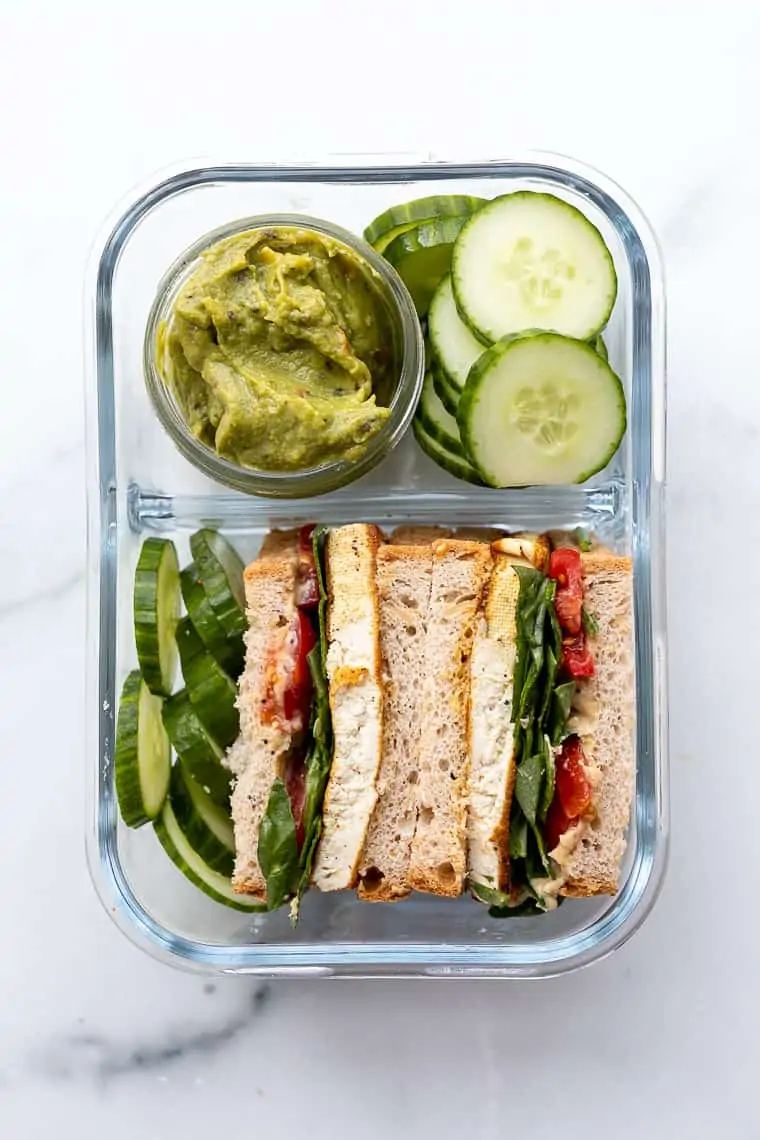 overhead of a glass bento box with cucumber and guacamole sandwiches