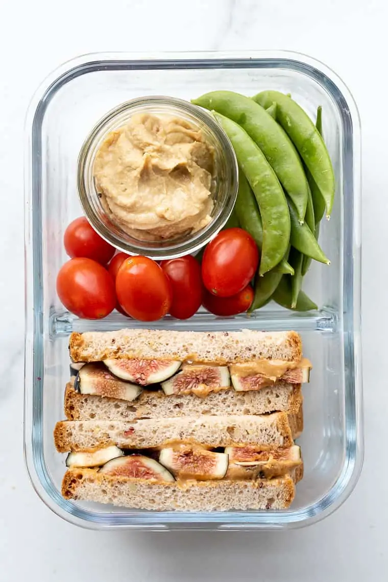 bento box with a fig and peanut butter sandwich, hummus and fresh veggies