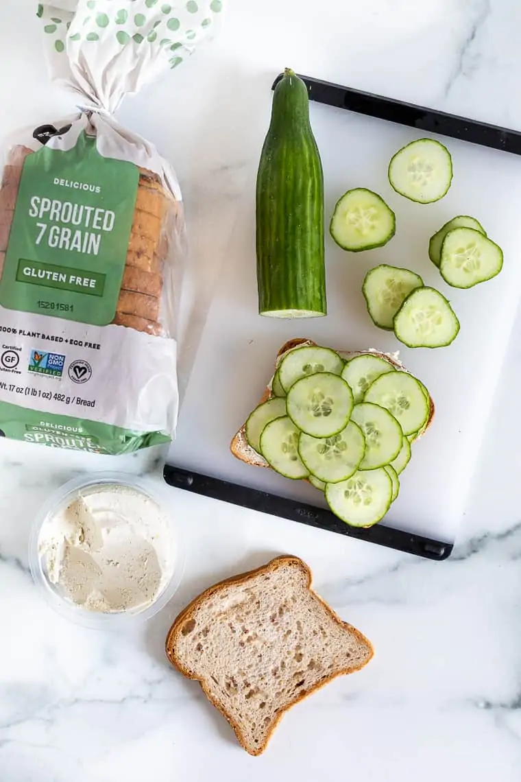 overhead of a loaf of grain bread and cucumbers on a cutting board