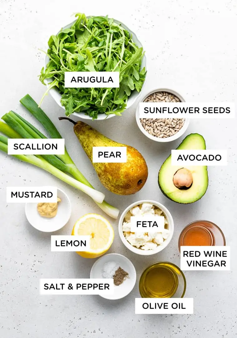 ingredients for salad with arugula, avocado, feta, pear, scallion