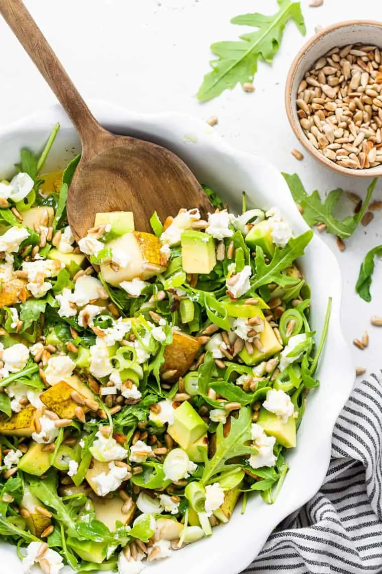 white bowl of arugula salad with pear and cheese