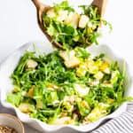 two wooden spoons tossing a salad with pear and avocado