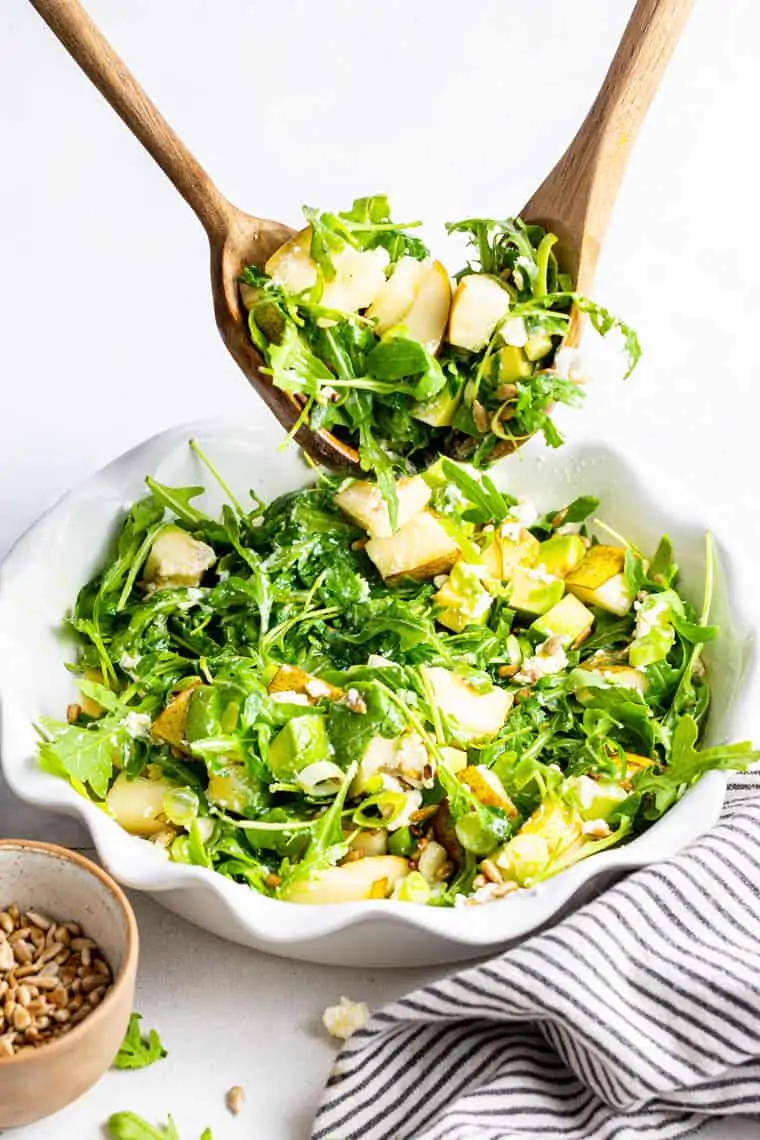 two wooden spoons tossing a salad with pear and avocado