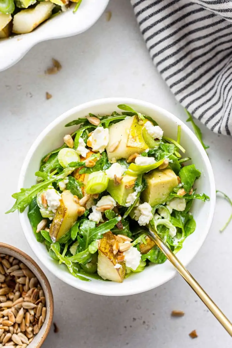 small white bowl of salad with pears, arugula, cheese and scallions