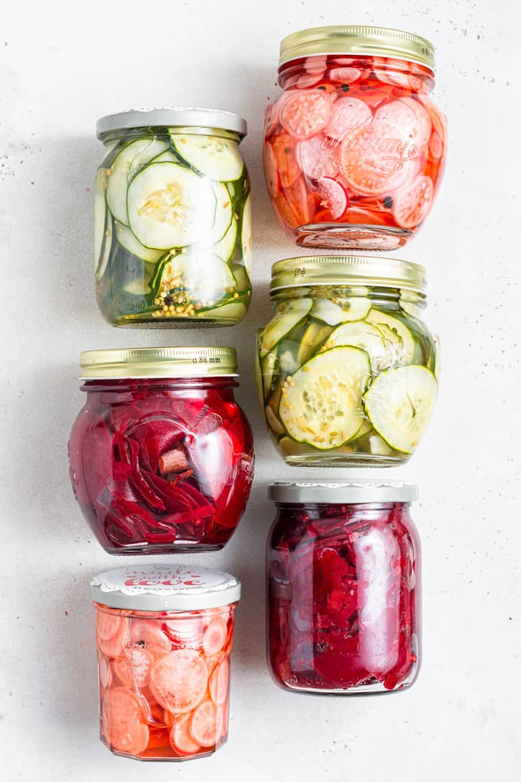 six jars of pickled cucumbers, red beets, and radishes