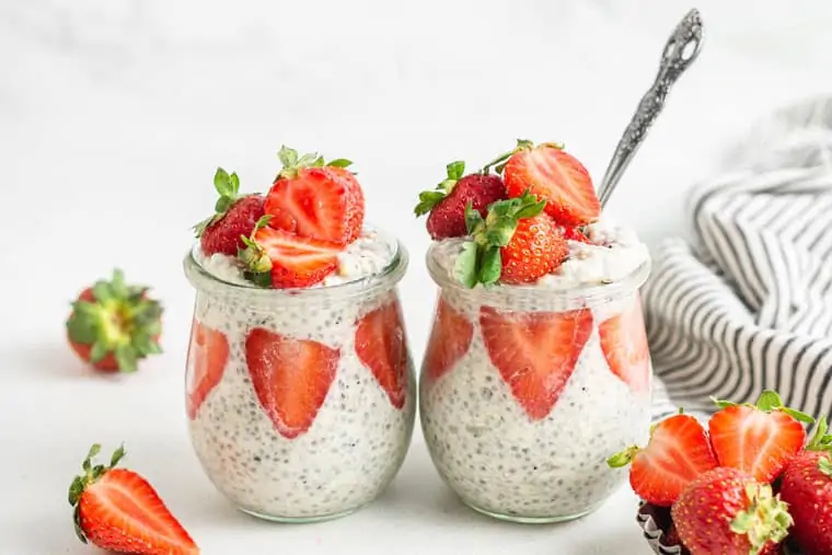 two glass jars of strawberry overnight oats with a silver spoon