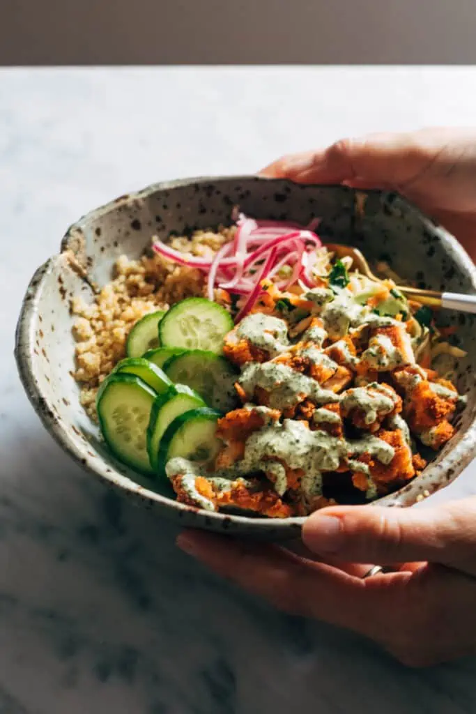Side view of pottery bowl in hands with chicken tikka and quinoa