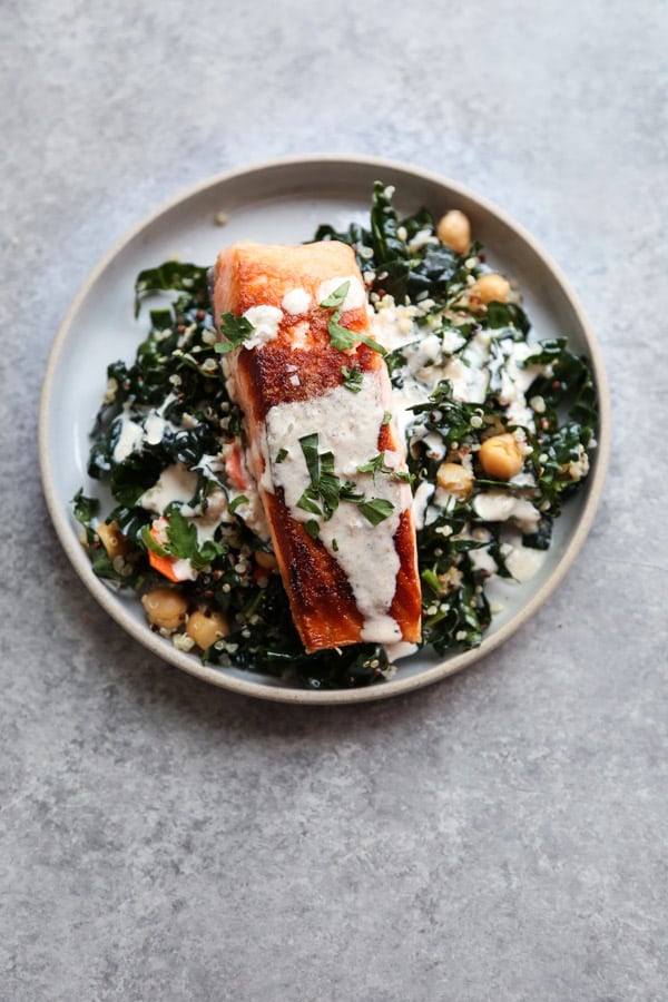 Overhead view of seared salmon on top of kale and quinoa, topped with a creamy white sauce