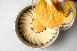 pouring cake batter into a pan with apple slices