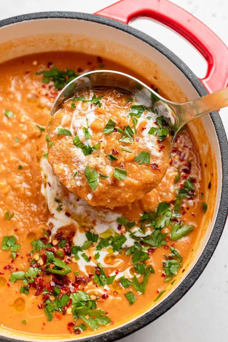 ladle full of red lentil soup in a red pot