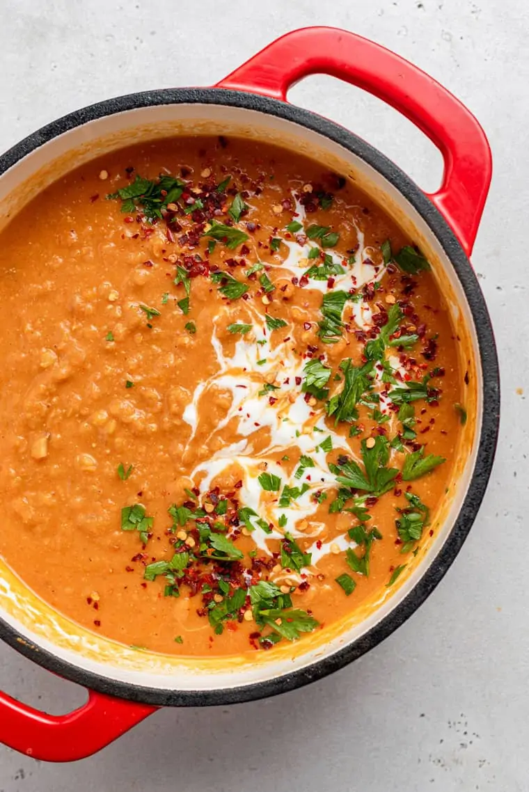 overhead of a pot of red lentil soup with cream and herbs