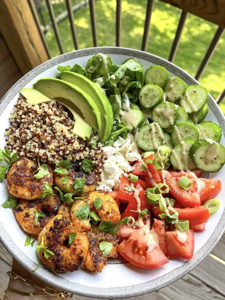 Overhead of quinoa bowl with sauteed shrimp, avocado, tomatoes and greens.