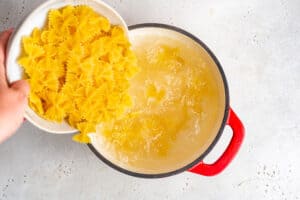 pouring bowtie pasta into a pot of boiling water