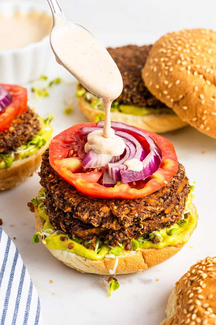 pouring sauce on a black bean burger with red onion and tomato