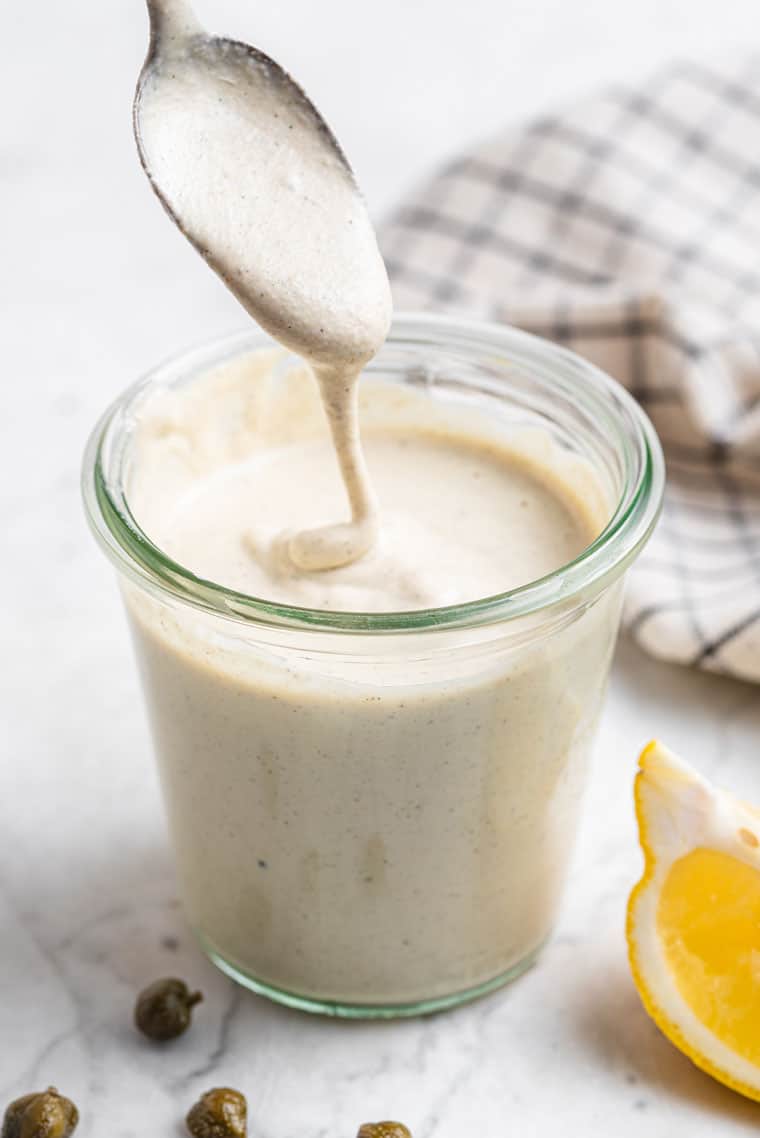 spoon in a jar of creamy vegan dressing with lemon