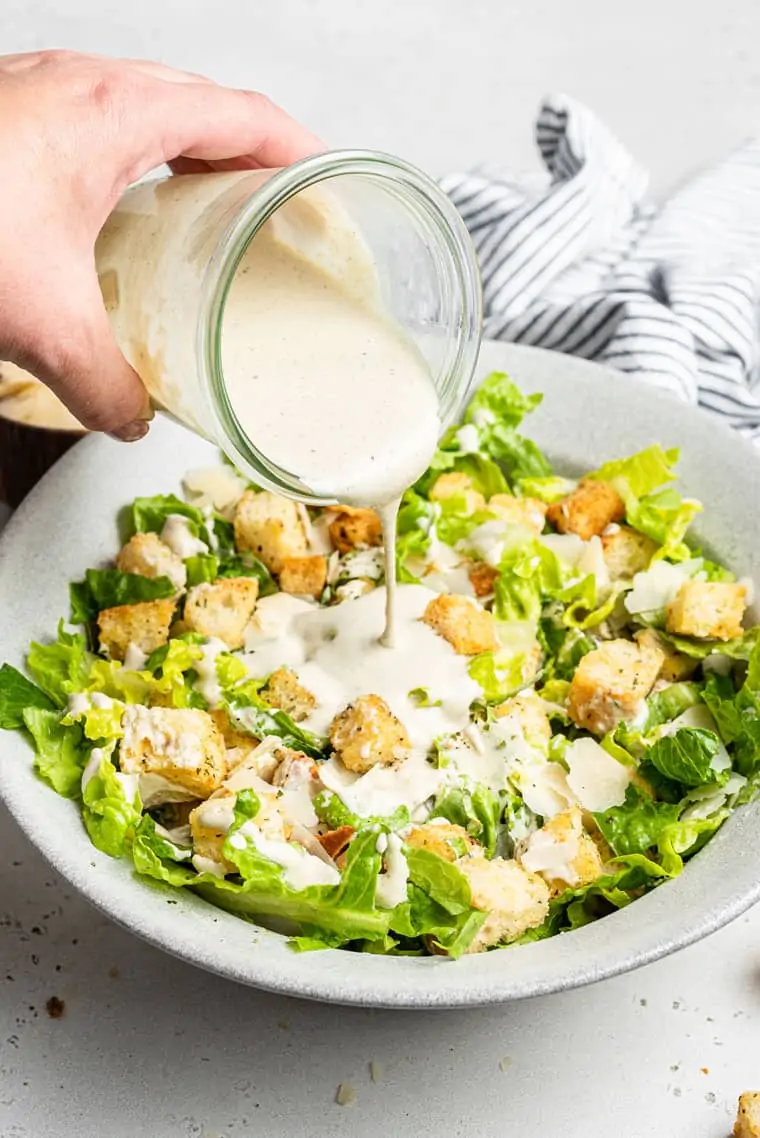 pouring dressing on a bowl of vegan caesar salad