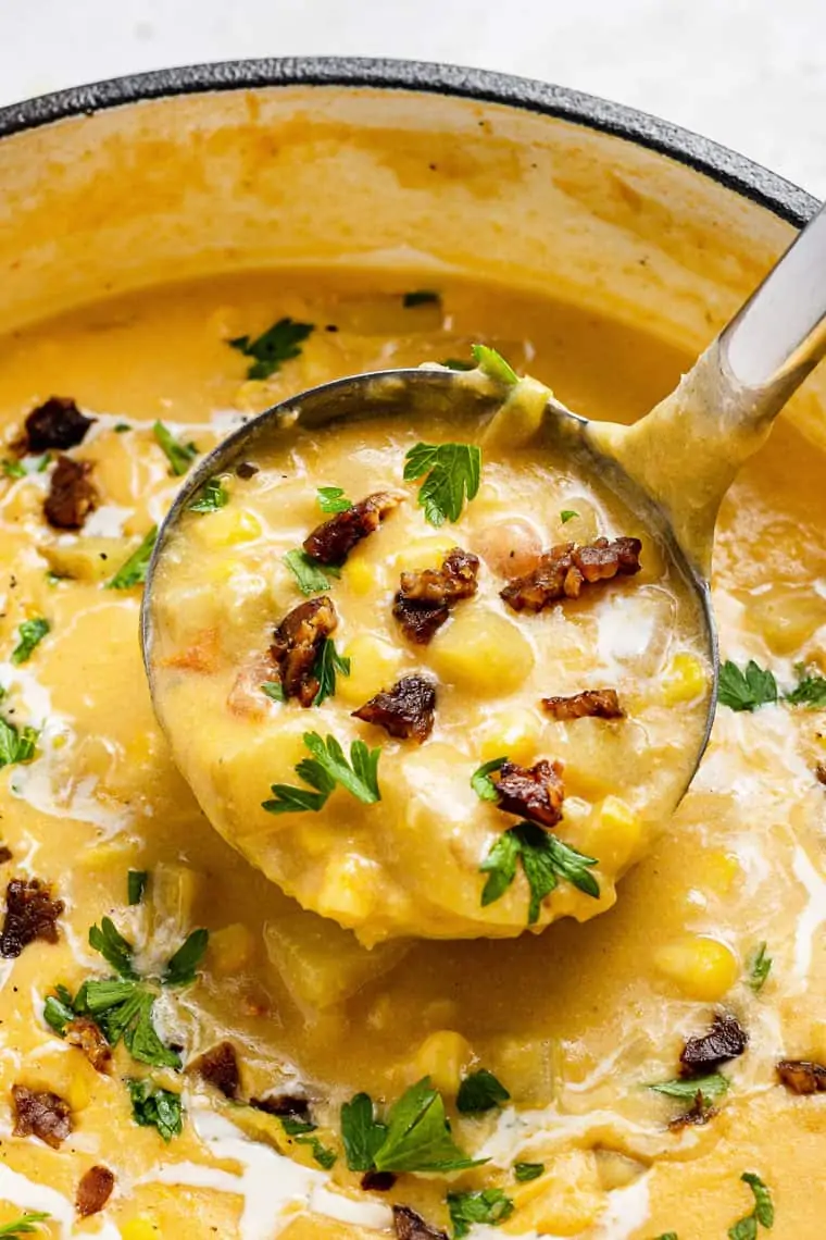 ladle of corn chowder with fresh herbs and tempeh on top