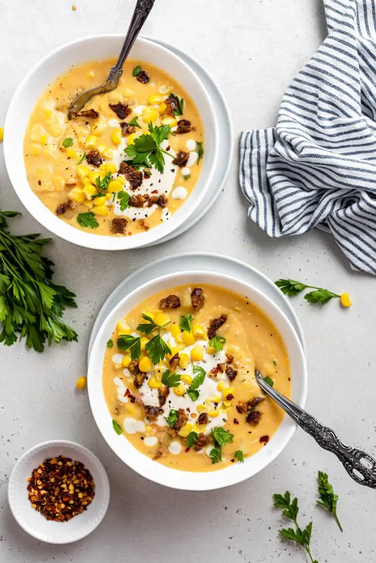 two white bowls of vegan corn chowder with fresh corn and herbs