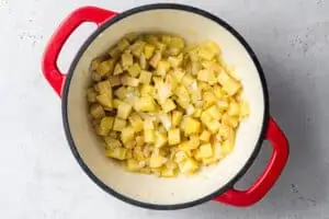 overhead of red pot with sauteed potatoes, onion and garlic for vegan corn chowder