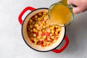 overhead of adding vegetable broth into red pot to make vegan corn chowder