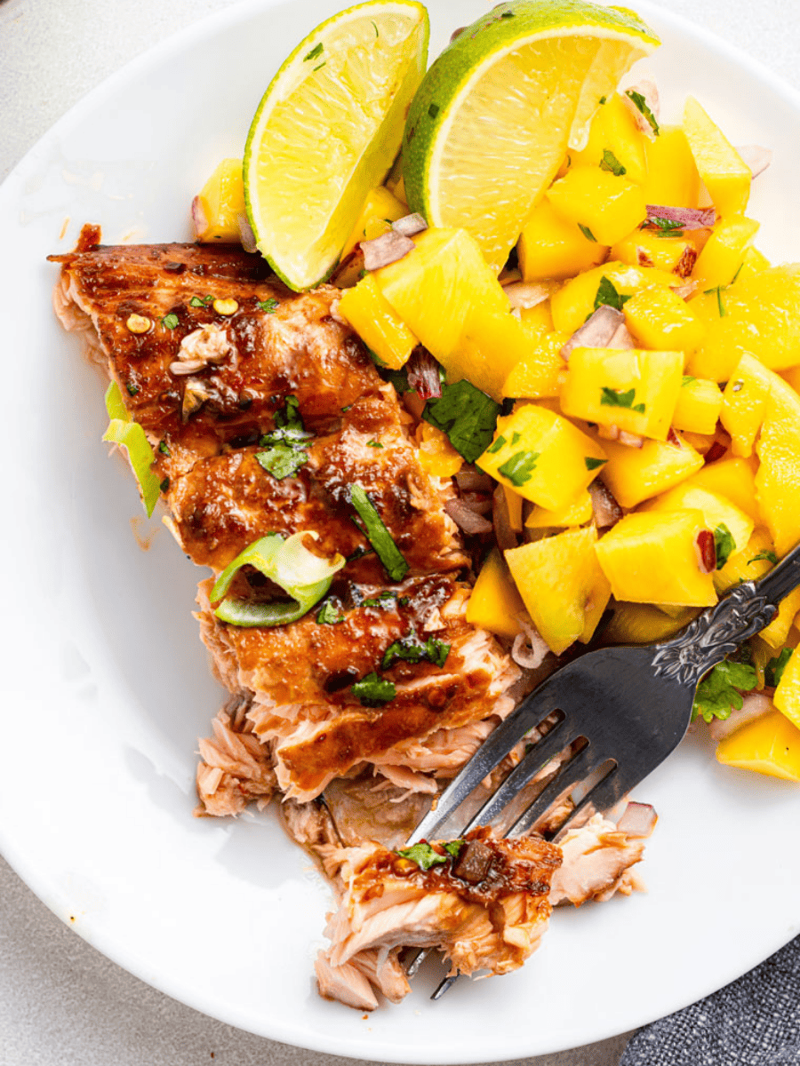 Fork piercing piece of firecracker salmon on plate with mango salsa