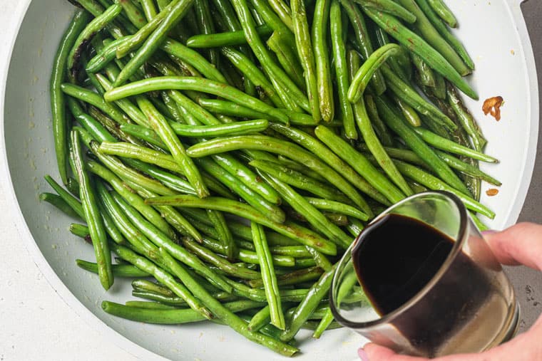 pouring tamari into pan with sauteed green beans