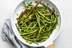 overhead of sauteed garlic green beans in a white pan with almonds and wooden spoon