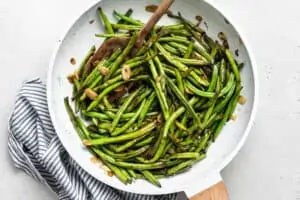 overhead of sauteed garlic green beans in a white pan with almonds and wooden spoon
