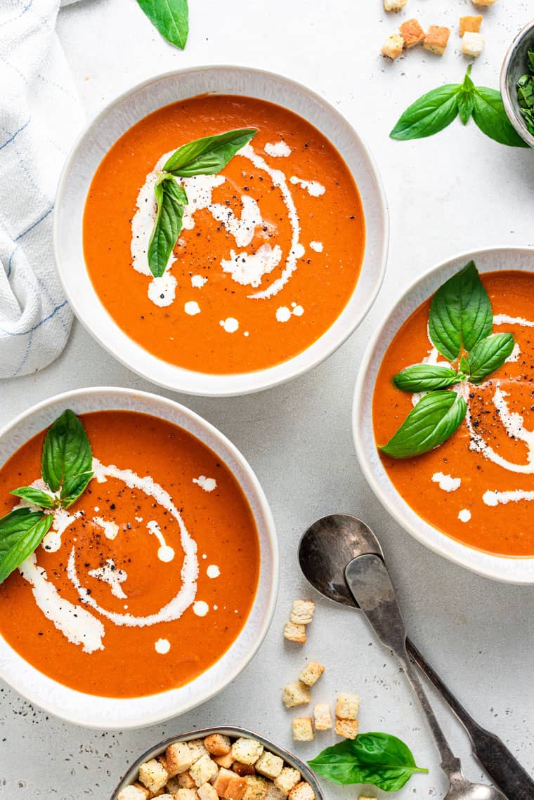 three bowls of tomato soup with cream on top