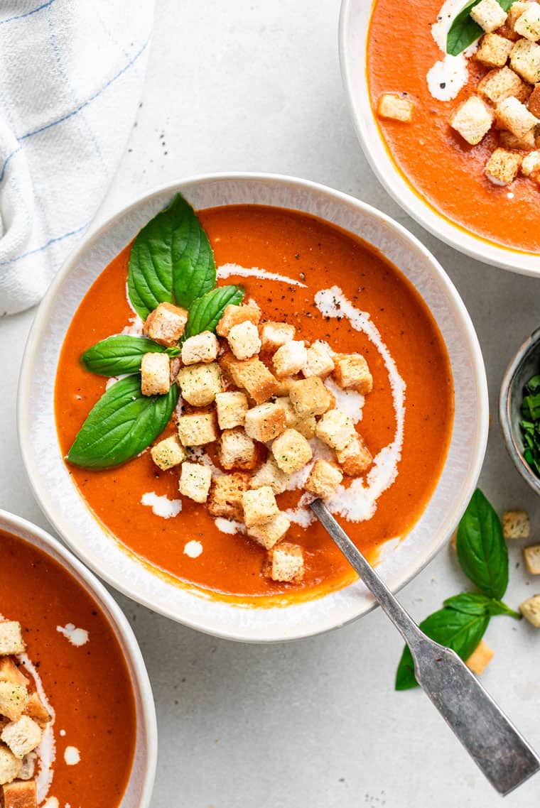 three bowls of tomato soup with basil and croutons