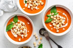 three bowls of tomato soup with croutons on top