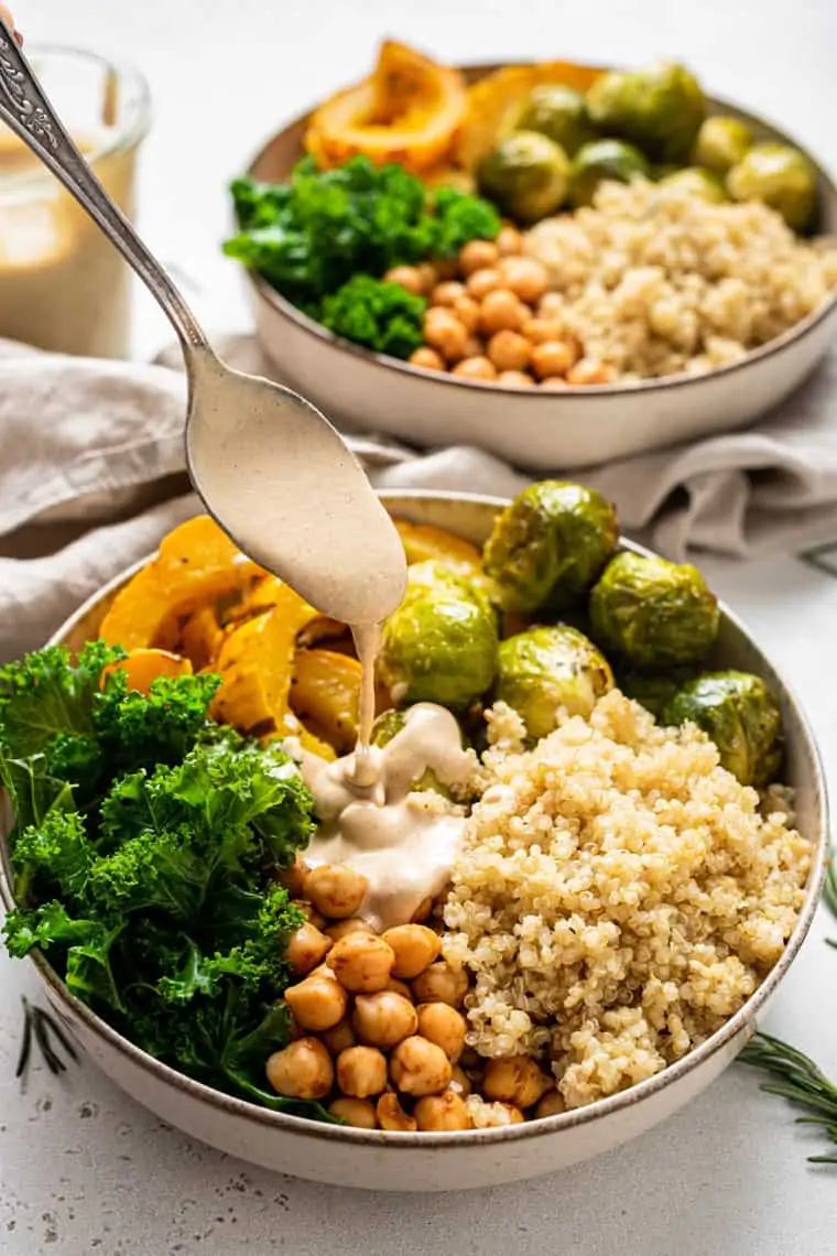 bowl with quinoa, kale and fall vegetables with dressing poured on