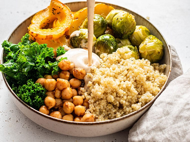 pouring dressing onto a quinoa bowl with squash and brussels