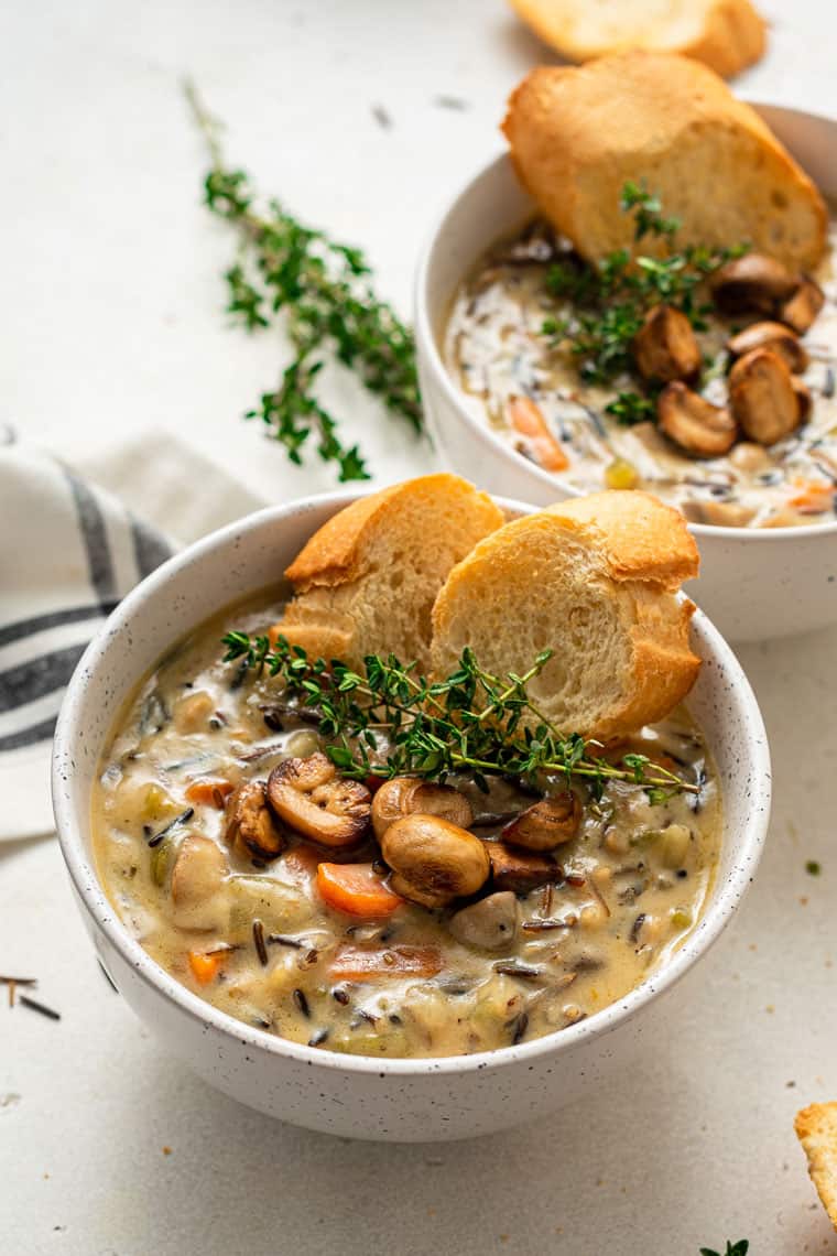 two bowls of wild rice and mushroom soup with bread slices