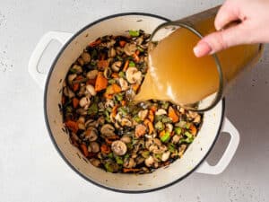 pouring broth into a pot with rice and vegetables