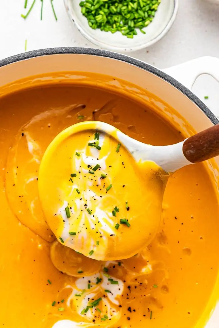 ladle of sweet potato soup with chives and cream