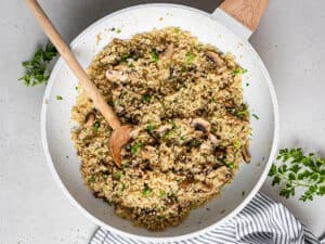 skillet stirring quinoa and mushrooms with a wooden spoon