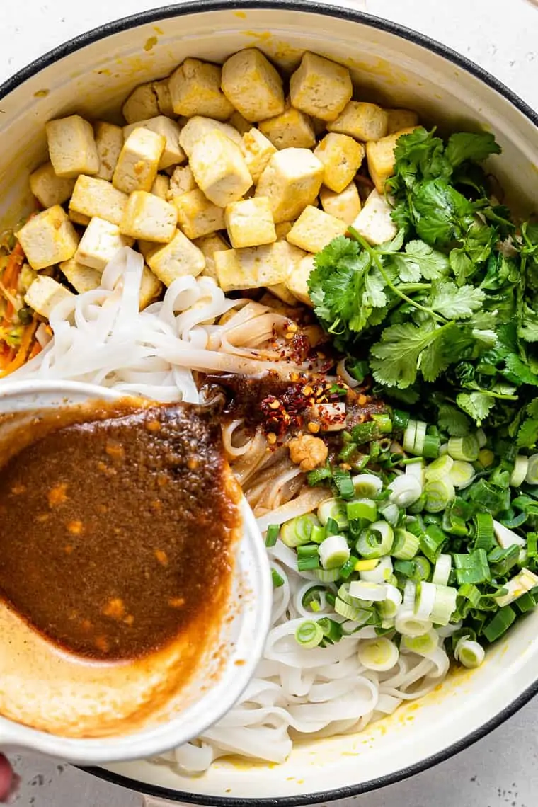 adding pad thai sauce to pot with tofu, noodles and herbs