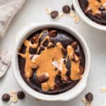 Overhead view of chocolate baked oatmeal drizzled with nut butter in a ramekin.