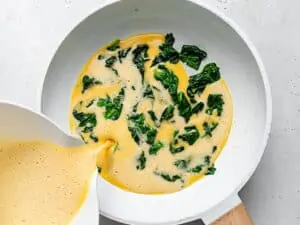 pouring whisked eggs into skillet with cooked kale