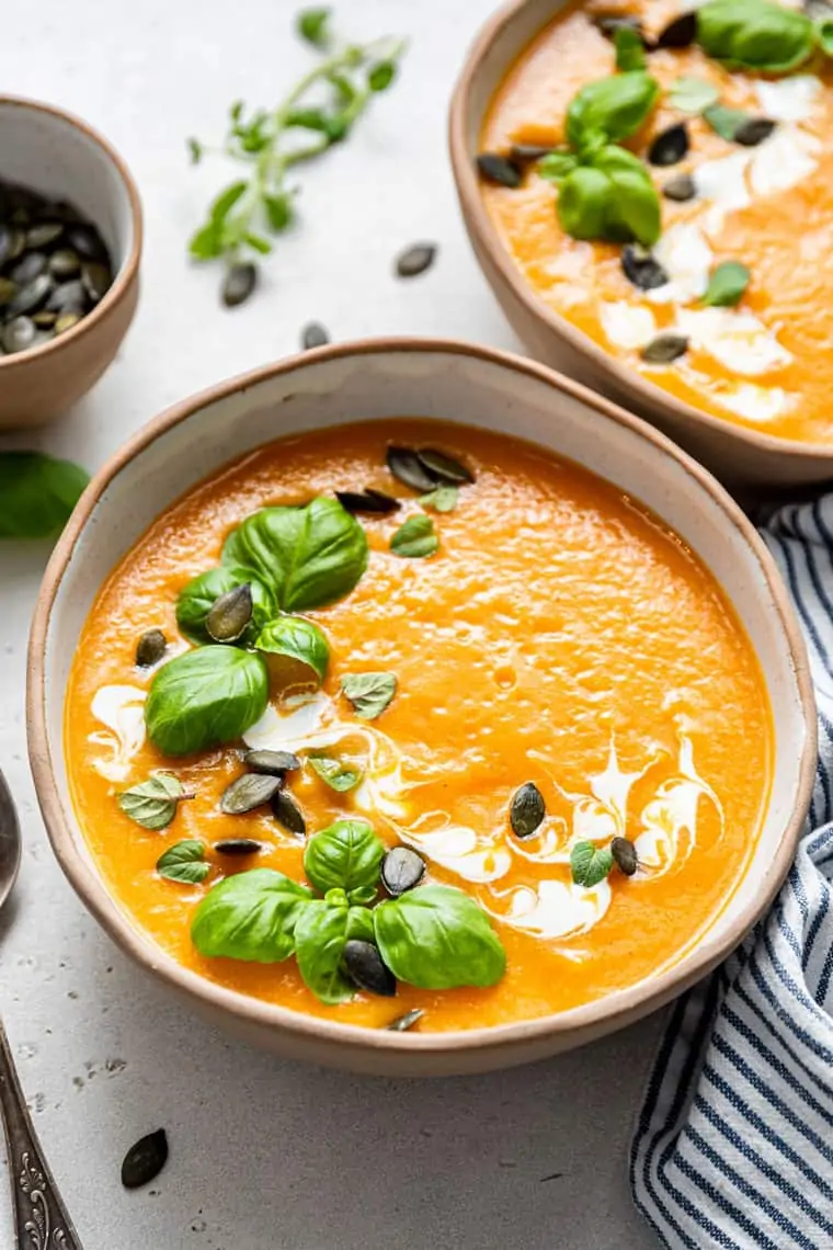 two bowls of butternut soup with basil and pumpkin seeds