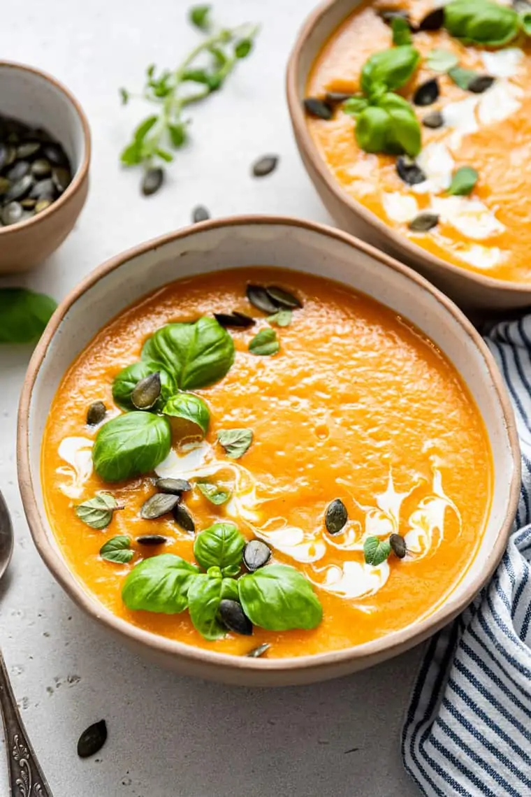Easy to make, super creamy and healthy, this is the best Roasted Vegan Butternut Squash Soup you'll ever taste. two bowls of butternut soup with basil and pumpkin seeds