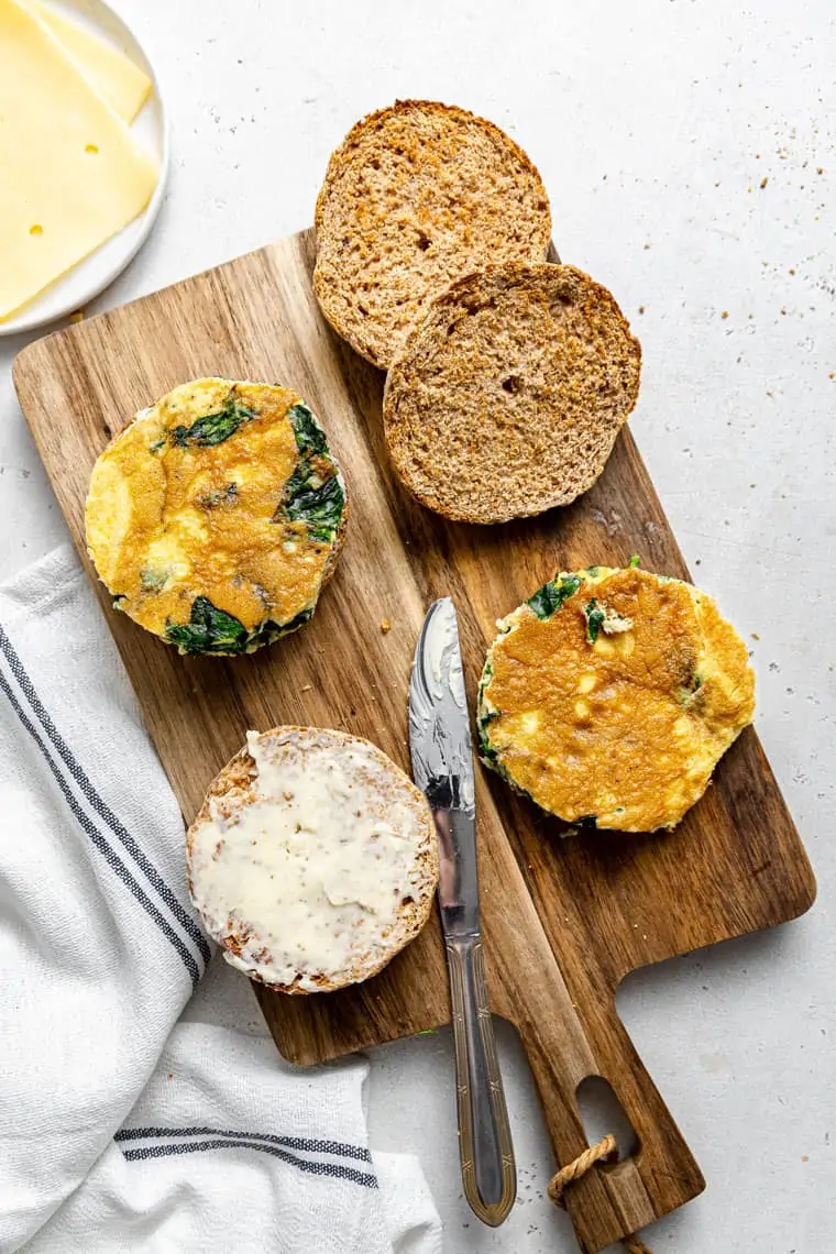 spreading butter on english muffins for breakfast sandwich