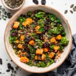 Overhead view of a bowl of farro salad with kale and sweet potato, next to a small bowl of pumpkin seeds.