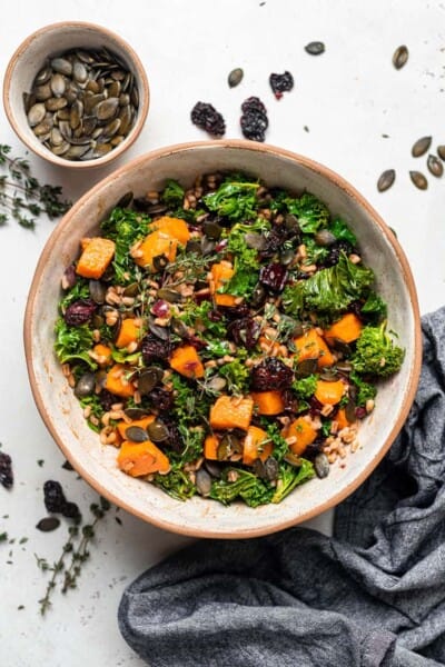 Overhead view of a bowl of farro salad with kale and sweet potato, next to a small bowl of pumpkin seeds.