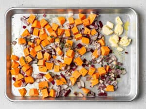 Diced sweet potato, onion, and garlic cloves on a baking sheet.