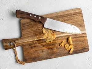 Overhead view of a knife resting on a cutting board next to partially mashed roasted garlic.