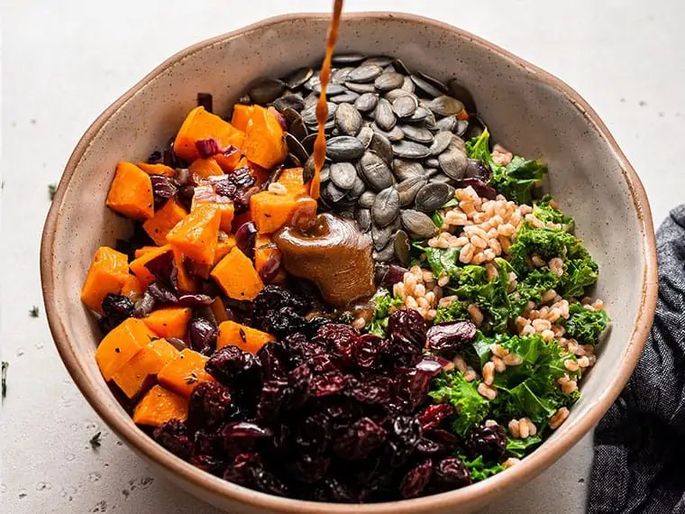 Dressing drizzled over a bowl of farro salad ingredients.