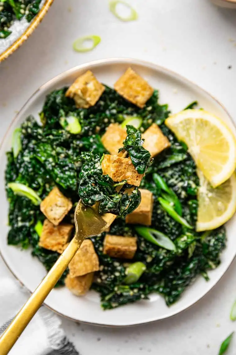 This 5-ingredient massaged kale salad is so easy to make, with a simple olive oil and lemon dressing. Enjoy as-is or add protein for a meal. tofu and massaged kale salad on a fork