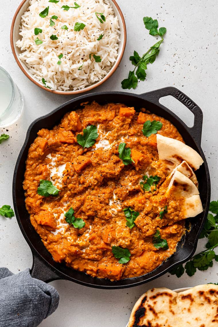 This creamy red lentil curry with sweet potatoes is a one-pot recipe that delivers lots of cozy comfort. It's an easy, filling vegan dinner! skillet of red lentil curry with rice and naan on the side